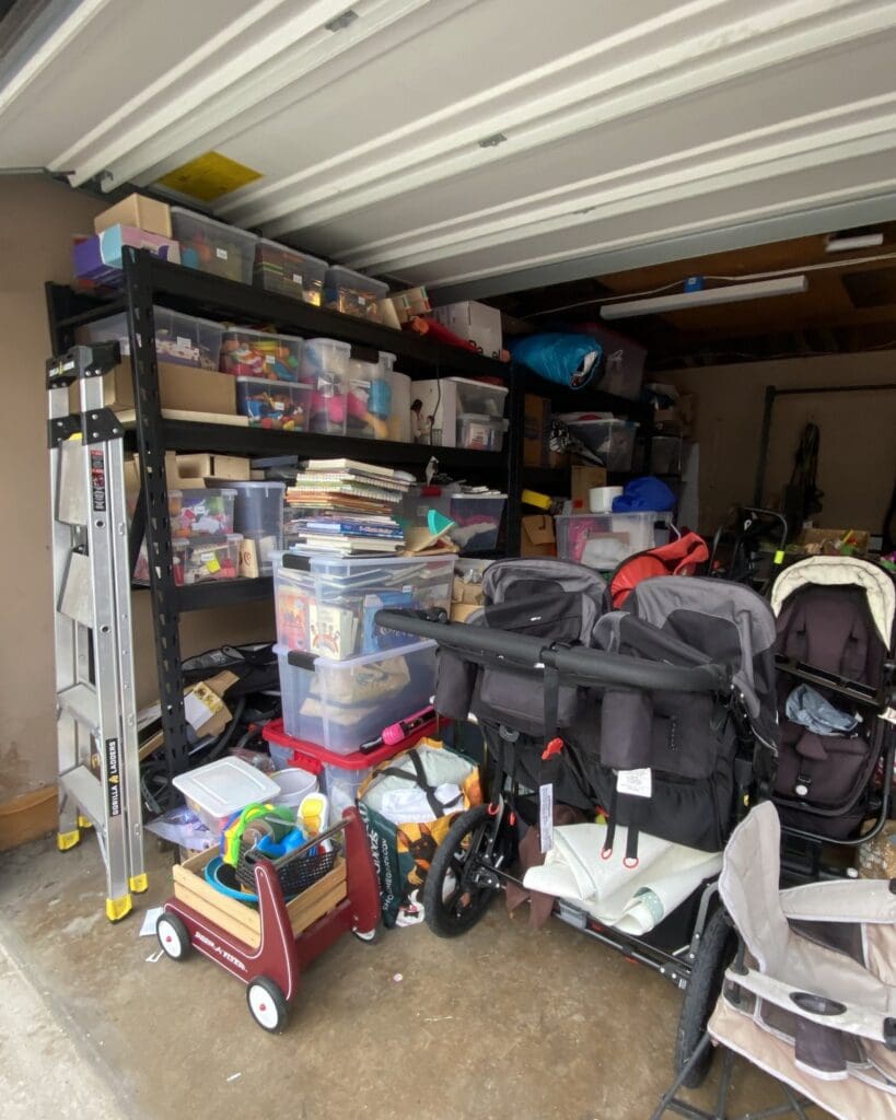 Garage before organizing in Woodland Hills, Los Angeles, seen from the open door, with strollers, a wagon, toys and bins crowding the shelving on the left wall
