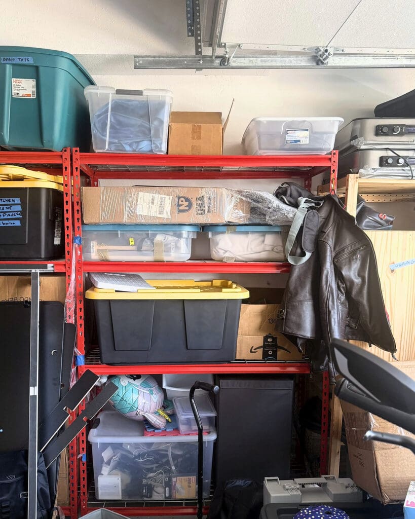 Red garage shelving before organizing, crowded with mixed bins, bags and loose items, Anaheim home