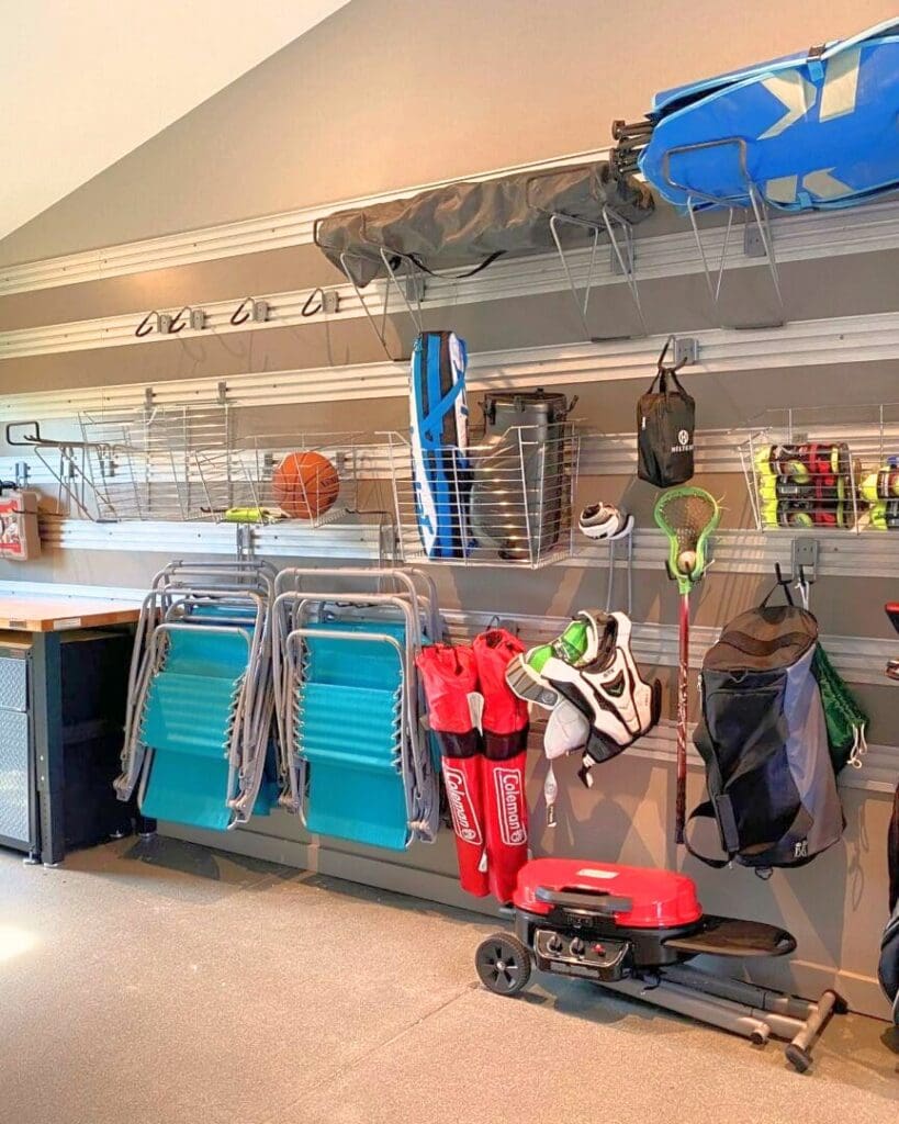 Same garage slat wall after organizing, with lawn chairs hung in a row, wire baskets for balls, lacrosse gear and the grill tucked against the wall