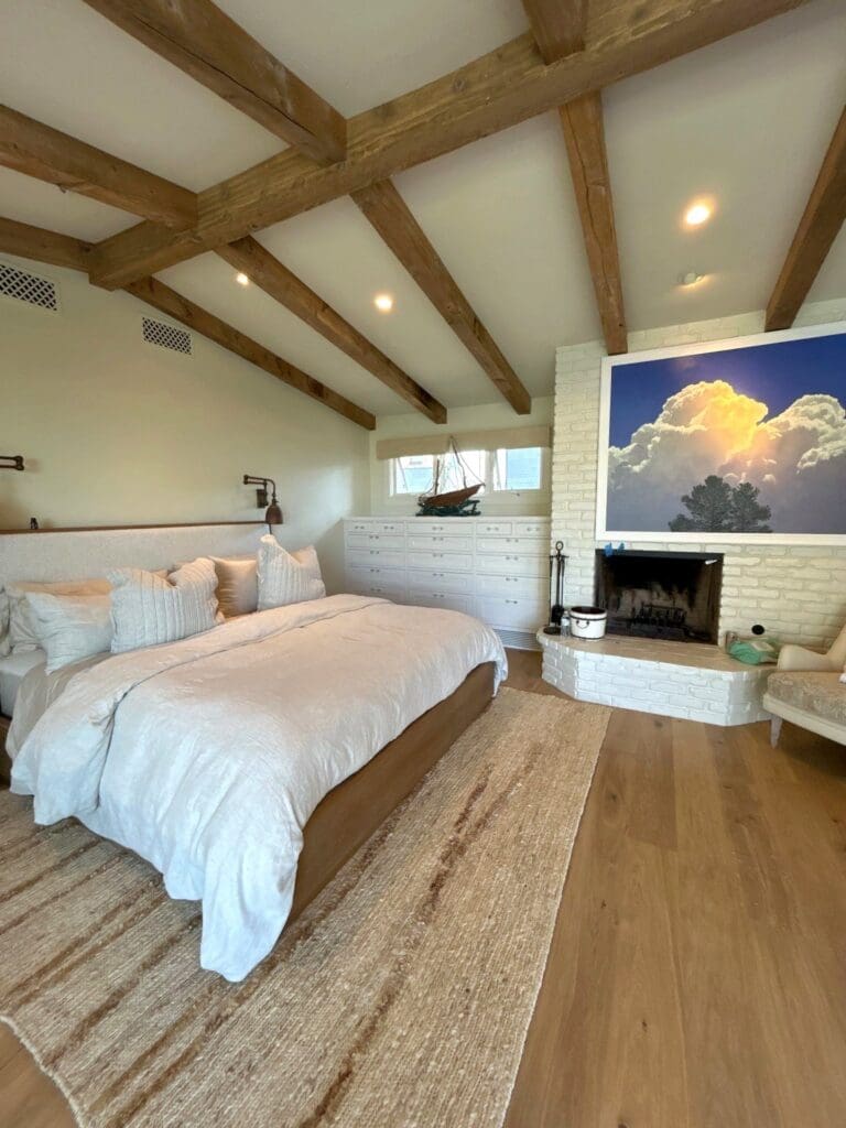 Calm guest-ready bedroom with crisp white bedding, wood beams, and a fireplace in a Southern California home