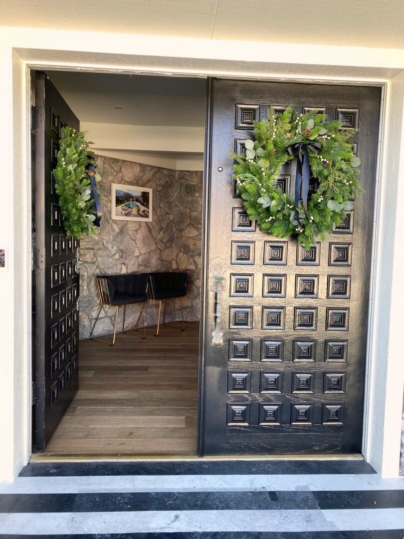 Black double front doors dressed with matching fresh greenery wreaths tied with black ribbon, holiday decorating by Simply Luxe