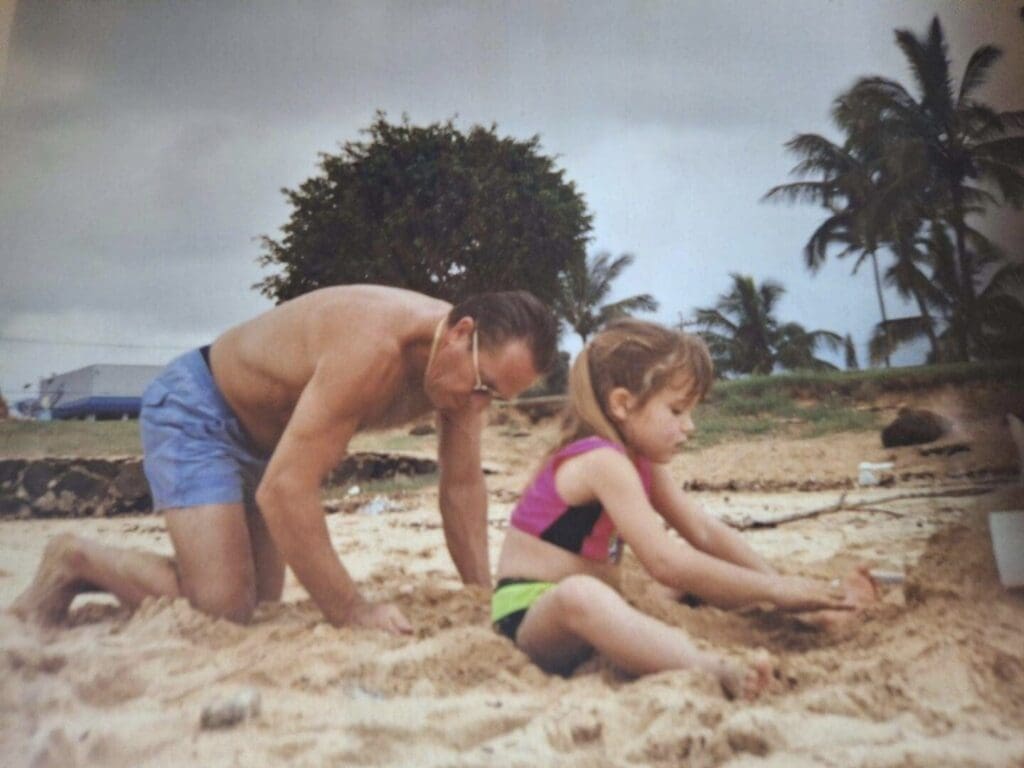 A man and a child playing together on a sandy beach.