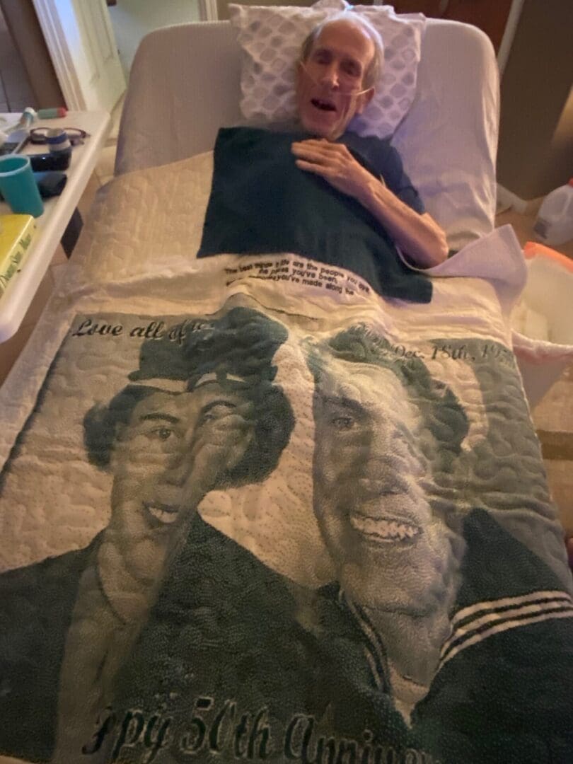 Person lying in bed covered with a blanket featuring a printed large portrait of two people.