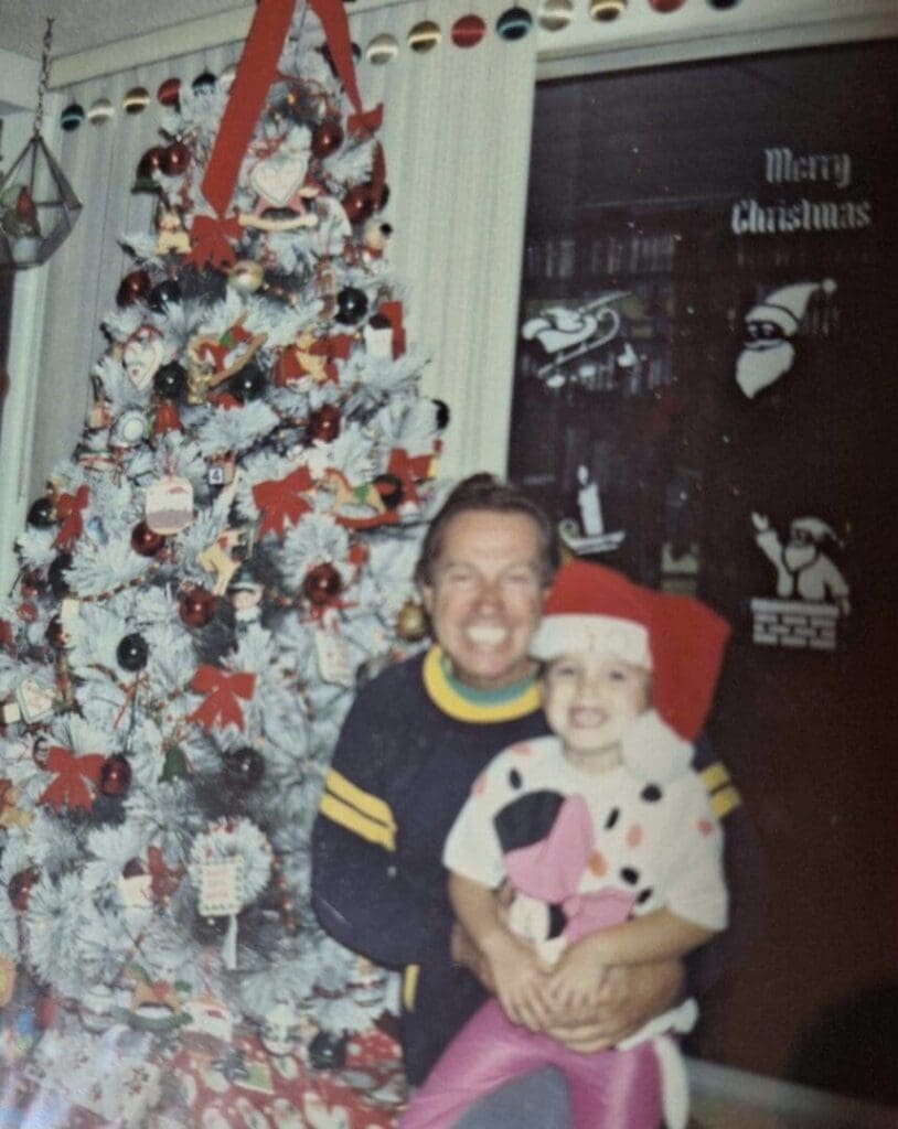 Two children smiling by a decorated Christmas tree.