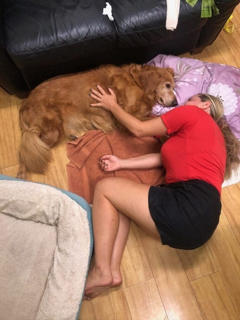 A woman lying on the floor hugging a large dog.