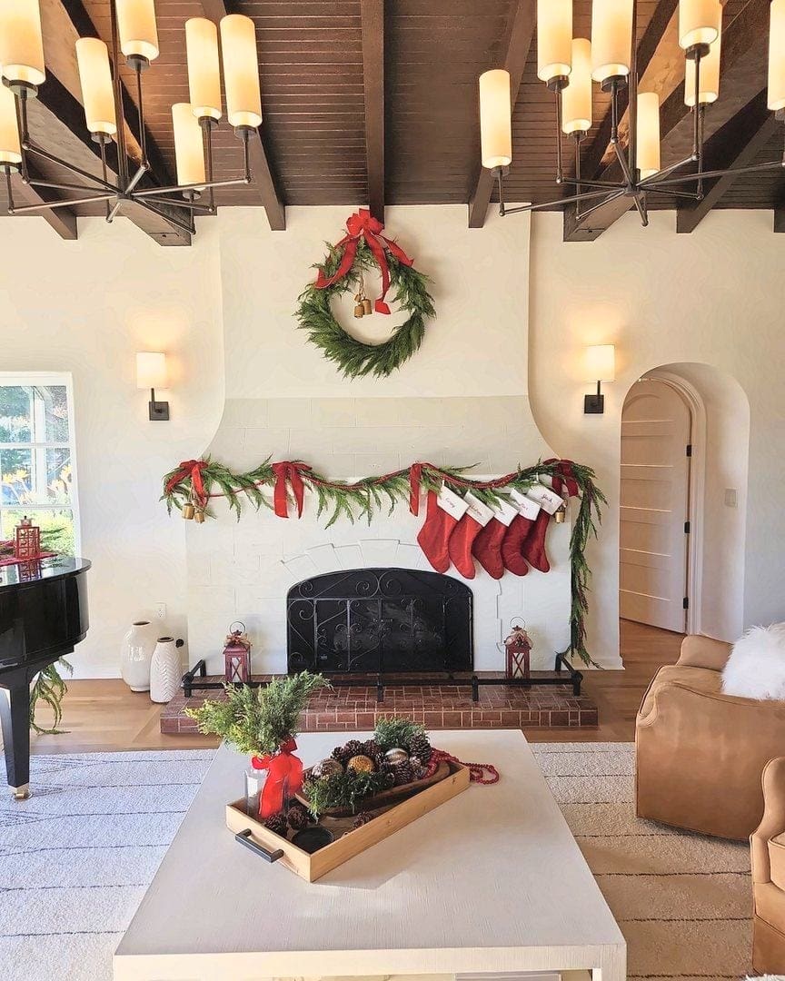 Living room fireplace dressed for the holidays by Simply Luxe with a wreath, garland, red stockings and a styled coffee table