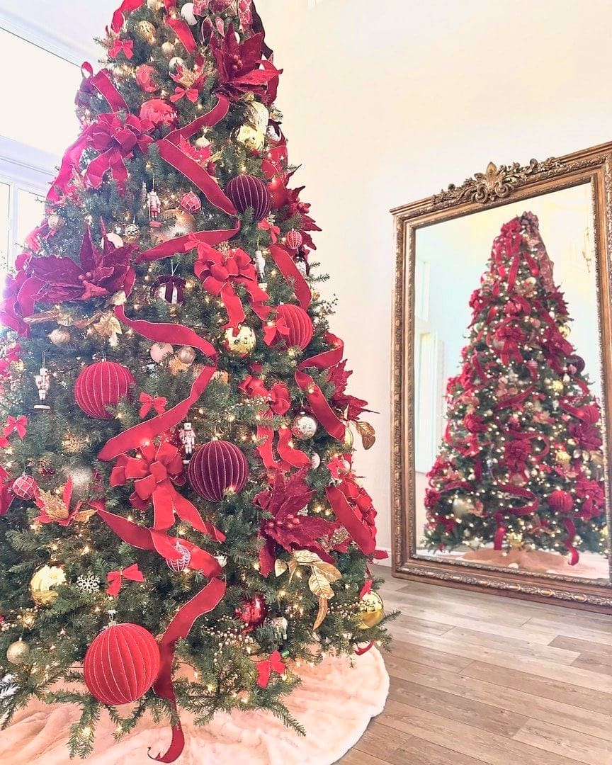 The same holiday tree after Simply Luxe decorating, layered in red and gold ribbon, poinsettia picks and oversized ornaments
