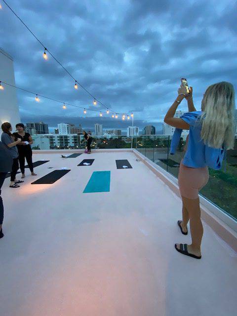 People practicing yoga on a rooftop at dusk with scenic city views.