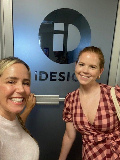 Two smiling women posing in front of a door with the iDesign logo.