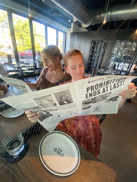 Two women reading a large newspaper titled 'Pandemic Ends At Last!'.
