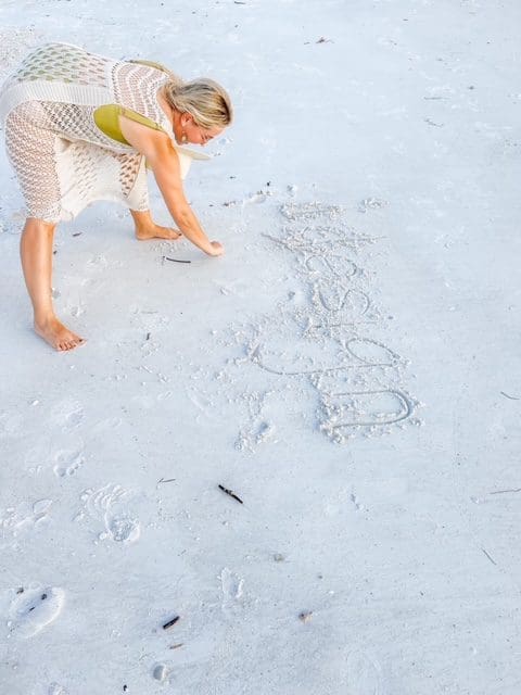 A woman draws a heart and the word 'LOVE' in the sand on a beach.