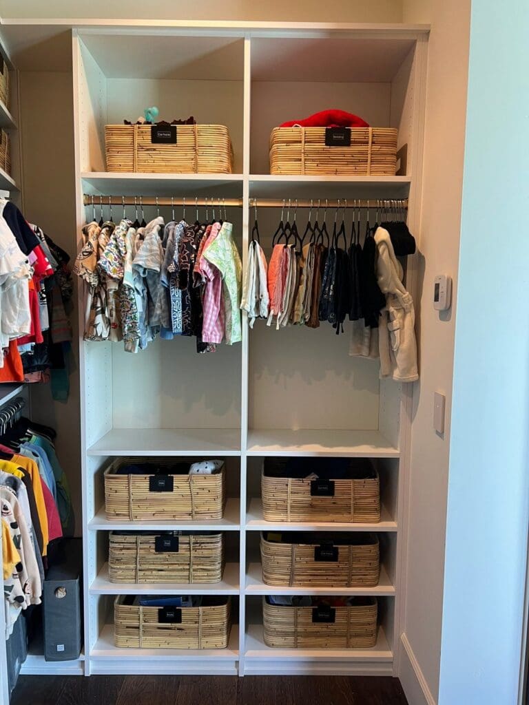 Kids closet with color-sorted hanging clothes and labeled woven baskets, organized in San Diego