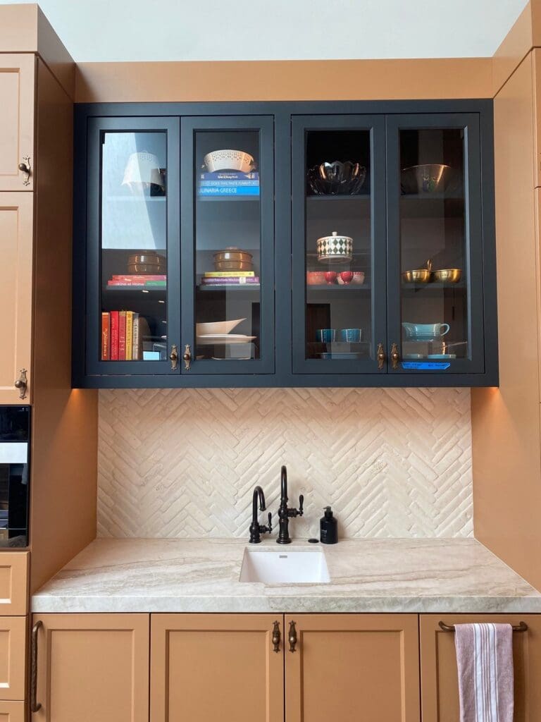 Black glass-front kitchen cabinets with cookbooks and serveware arranged by color, organized in San Diego