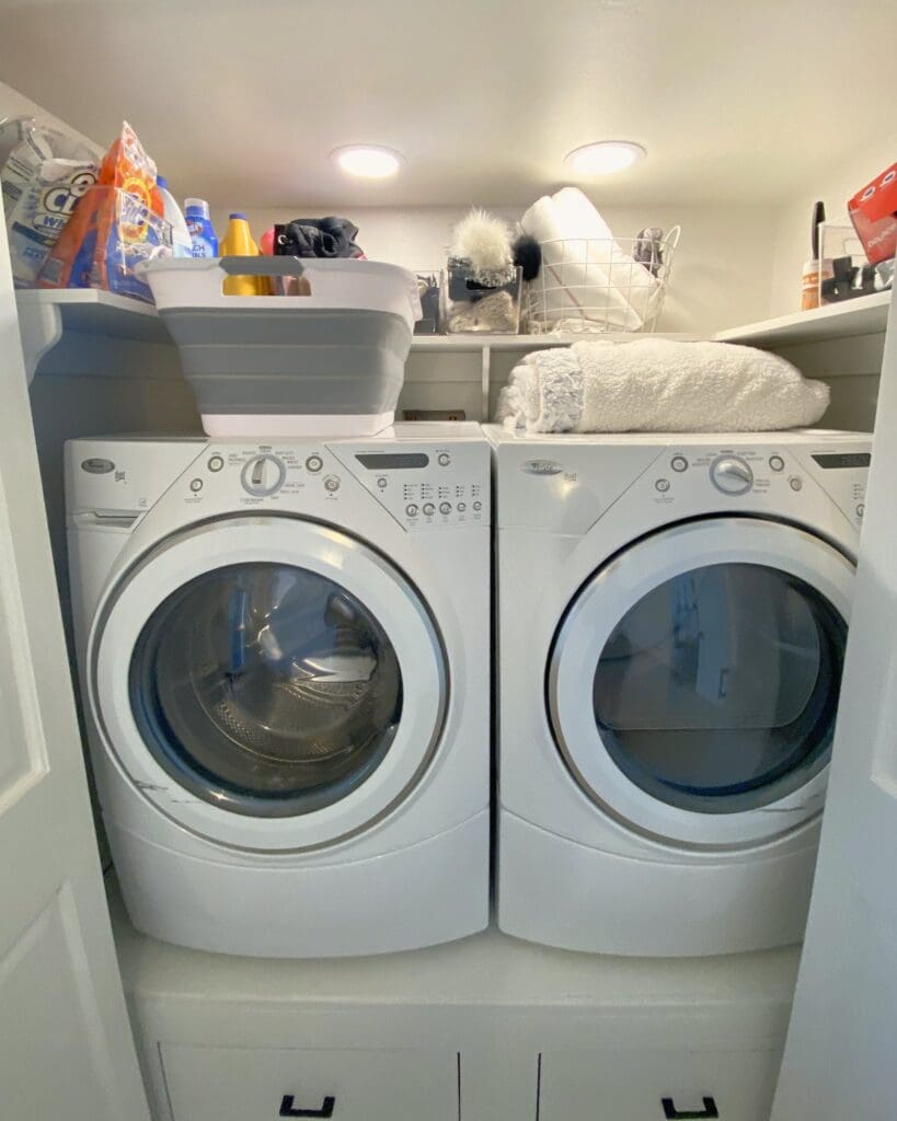 Laundry closet before organizing, with detergent, bags and towels piled on the shelf above the washer and dryer, Lake Arrowhead