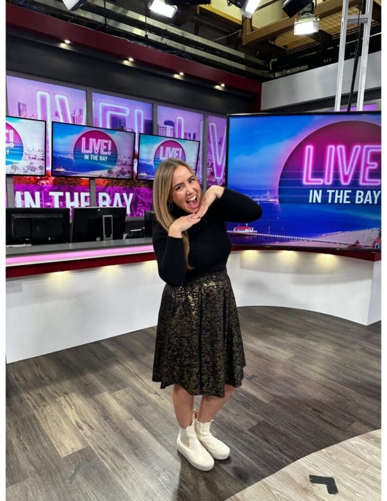 Live in the Bay woman in front of tvs with Live in the Bay written on