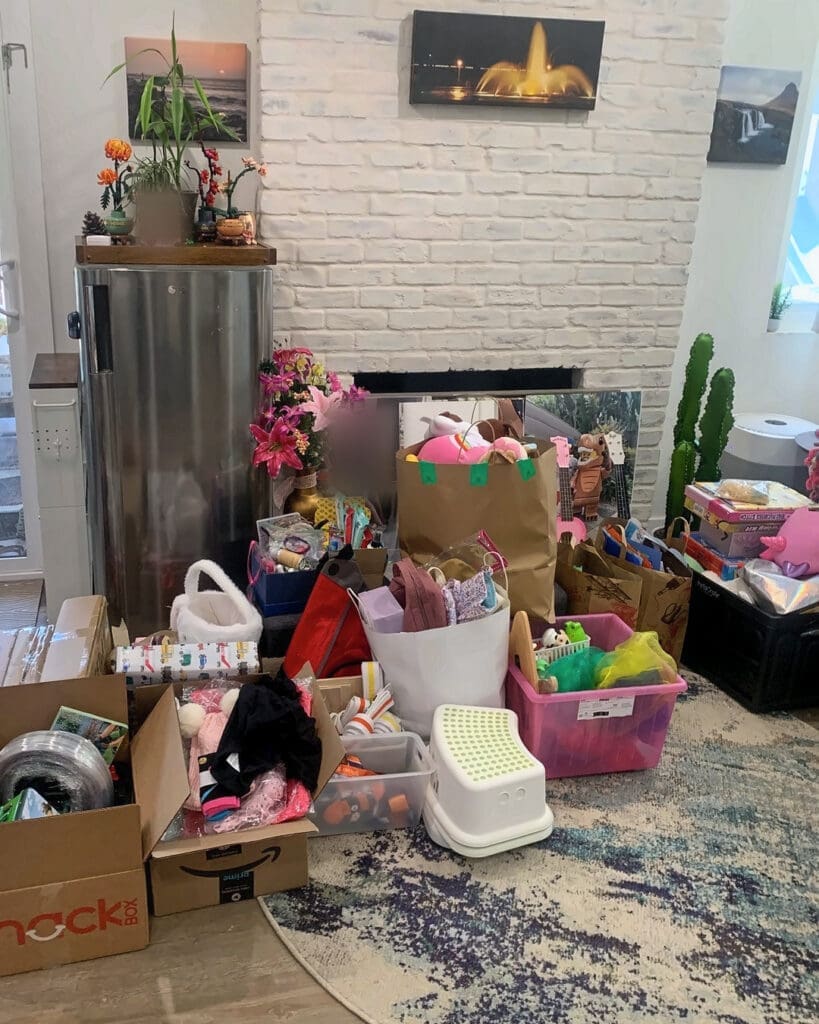 Living room before organizing, with bags, boxes and bins of toys piled in front of a white brick fireplace, Anaheim home
