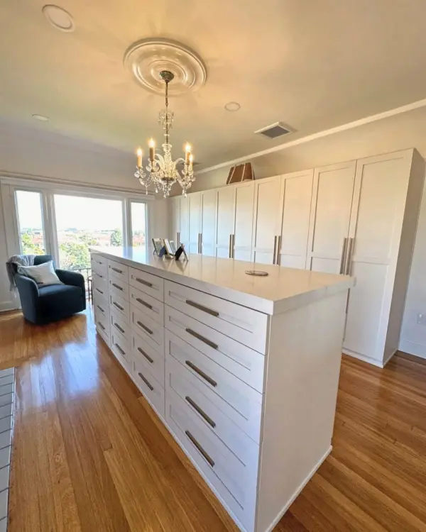Luxury walk-in closet room with white wardrobe wall, drawer island and chandelier, San Diego