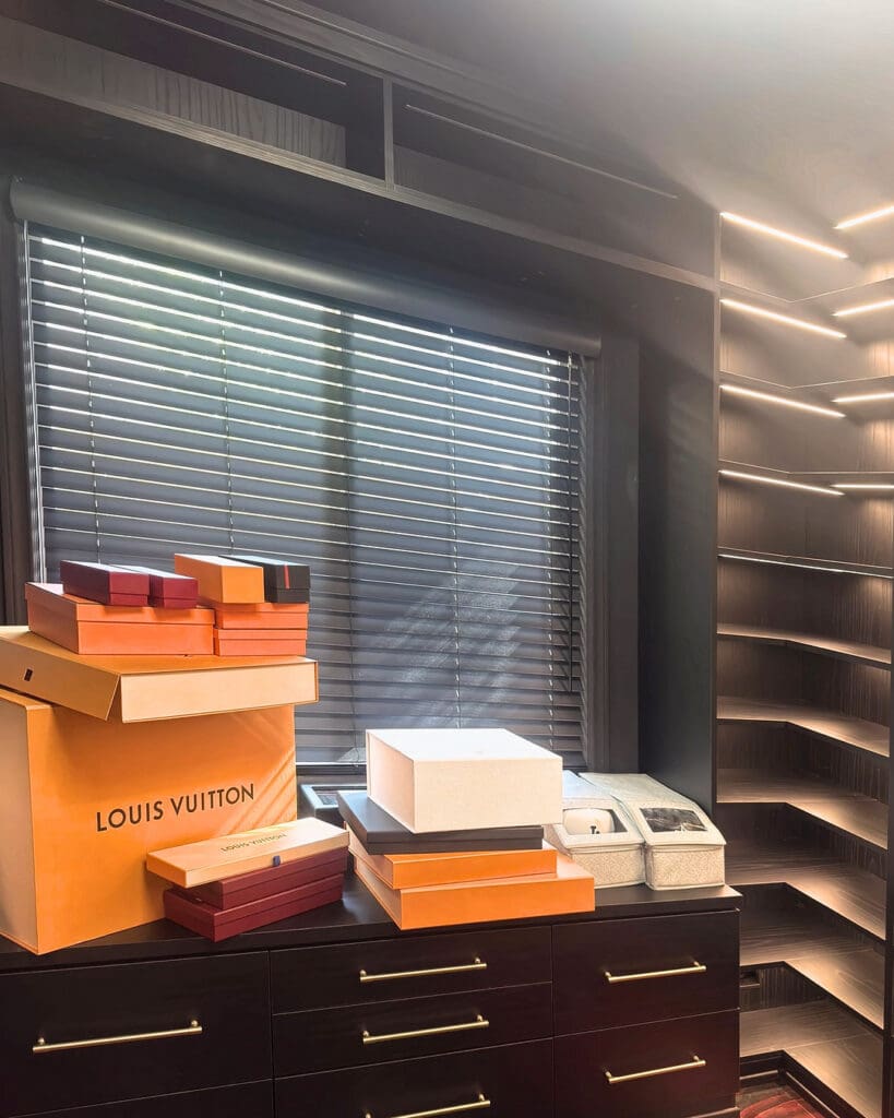 Men's walk-in closet before organizing, with designer shoe boxes piled on the dresser and empty display shelves, Costa Mesa home