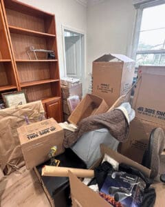 Moving boxes, bags and a chair piled in front of an empty bookcase on move in day, San Diego home
