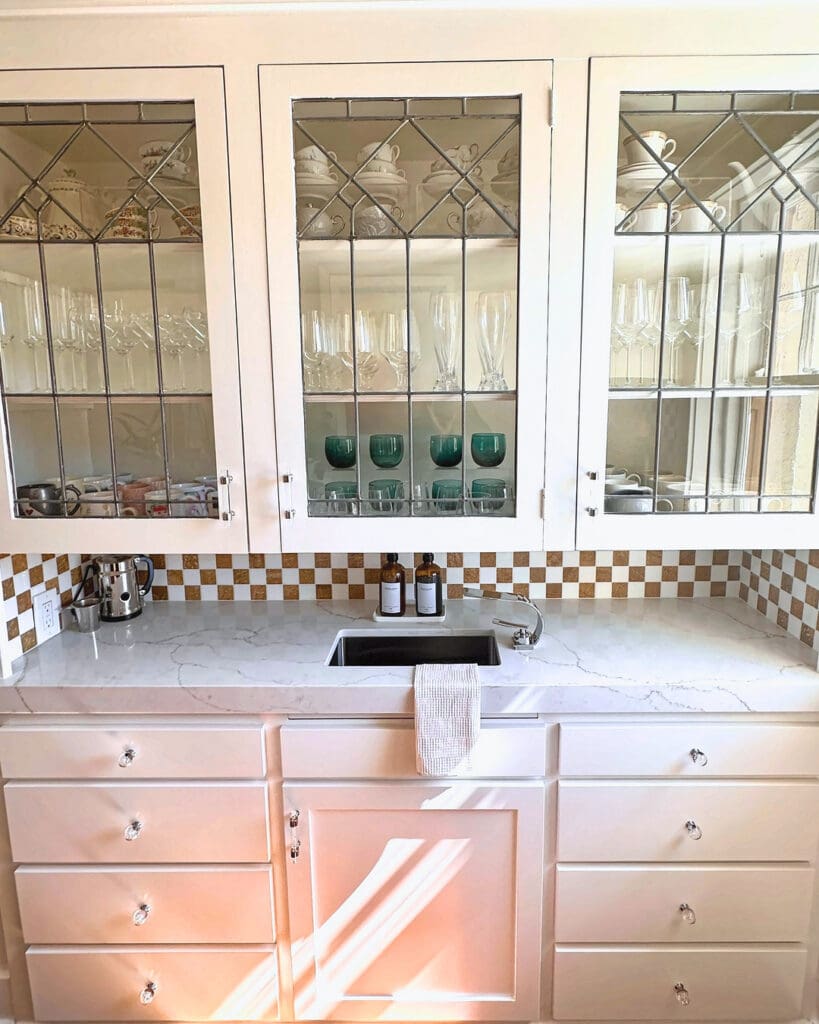 Same butler pantry after the Simply Luxe unpack, glass cabinets styled with stemware, green goblets and serving pieces, Orange County