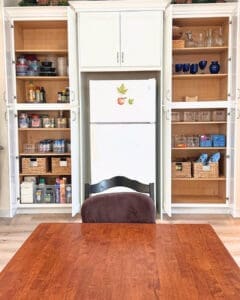Same kitchen built ins after the Simply Luxe unpack, shelves filled with glassware, pantry baskets and dry goods around the fridge, San Diego