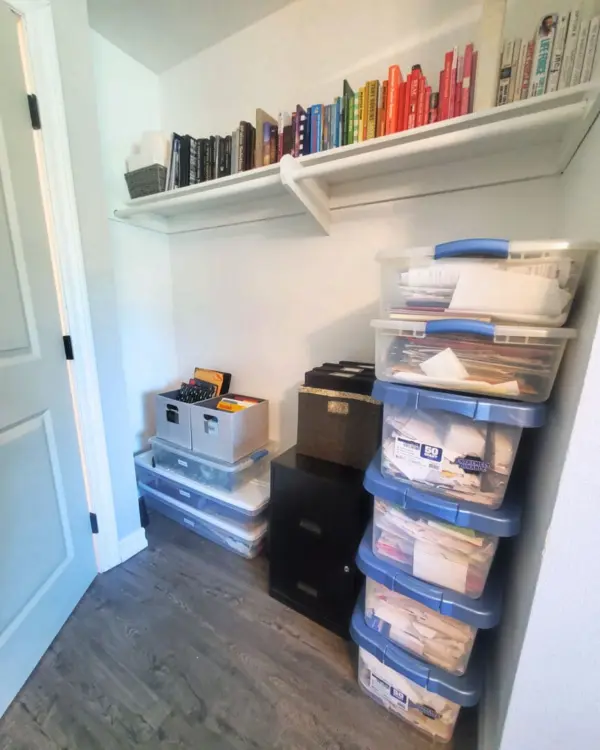 Office closet after organizing, with books by color on the shelf and stacked clear bins below