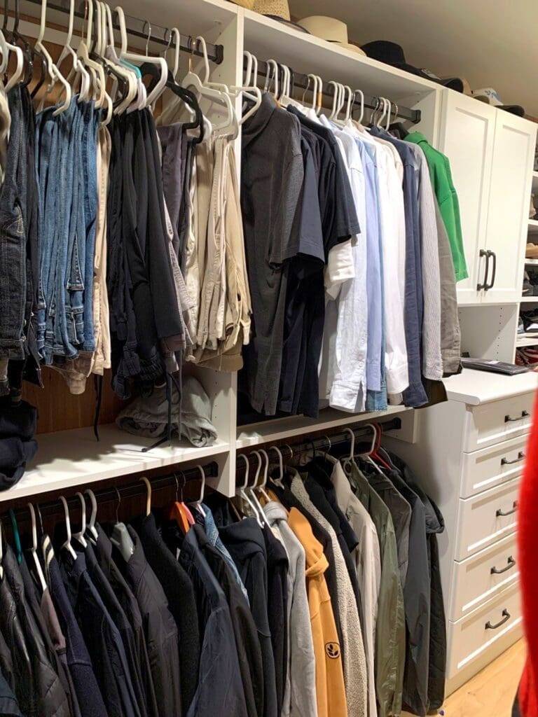 Organized walk-in closet with shirts and pants on matching hangers, sorted by color