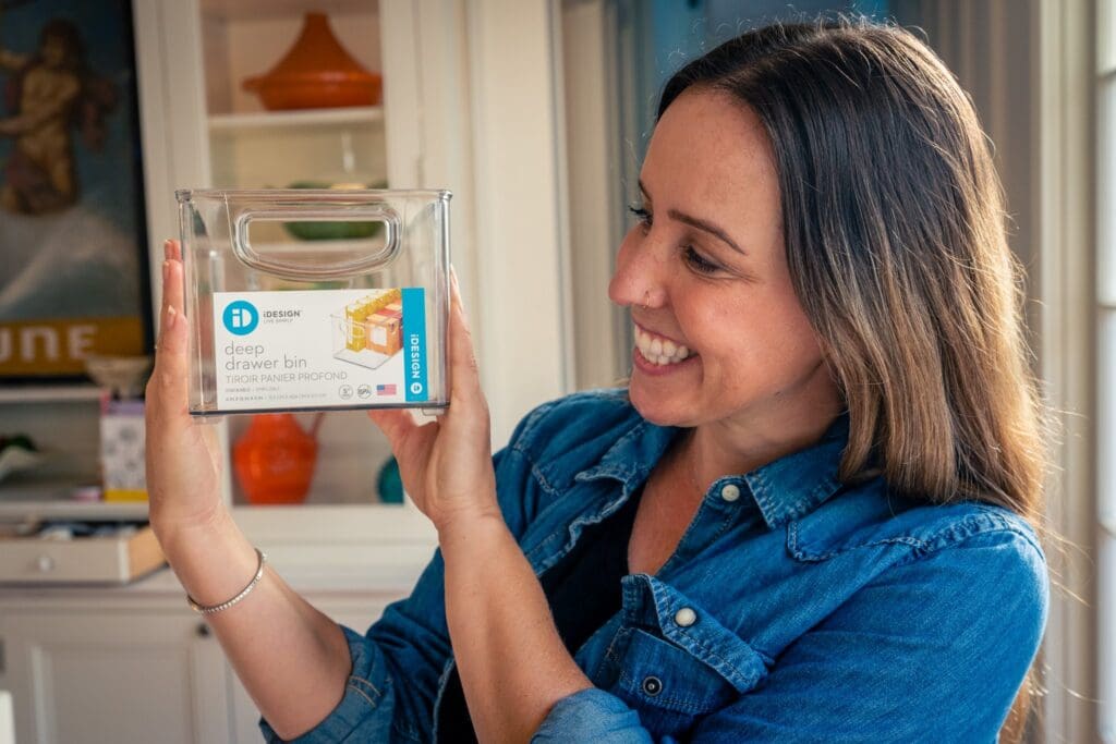 Smiling organizer holding up a clear labeled pantry bin in a styled kitchen