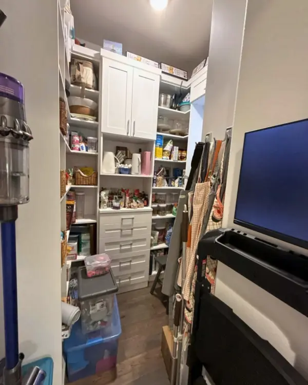 Walk-in pantry before organizing, with crowded shelves, a vacuum and clutter blocking the doorway, San Diego home