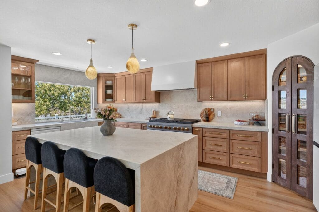Remodeled Orange County kitchen with a wood island, black stools, and arched pantry cabinets