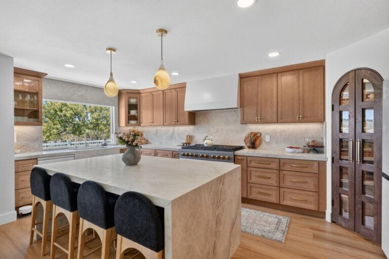 Remodeled Orange County kitchen with a wood island, black stools, and arched pantry cabinets