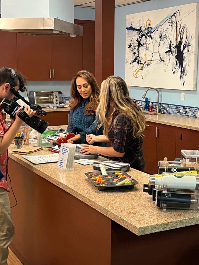 Two women filming a cooking session in a modern kitchen.
