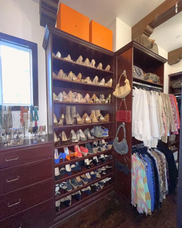 Walk-in closet shoe wall with heels lined up by style on dark wood shelves and handbags hung beside the hanging clothes, organized by Simply Luxe, Orange County