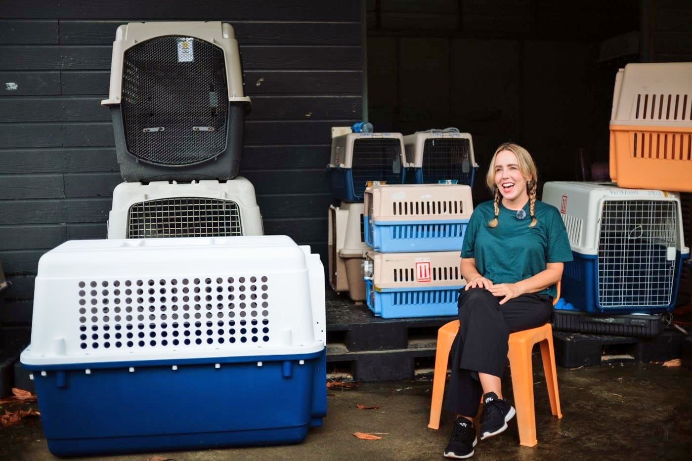Ryen Toft smiling on a stool surrounded by stacked pet travel crates during her Soi Dog Foundation Flight Buddy interview