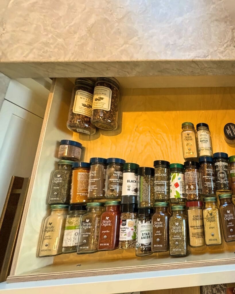Kitchen spice drawer before organizing, with spice jars tossed in loose rows across the drawer bottom, San Diego