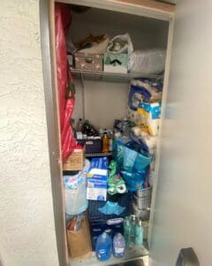 Orange County storage closet before decluttering, with paper towels, cleaning supplies, bags and boxes crammed onto wire shelves and the floor