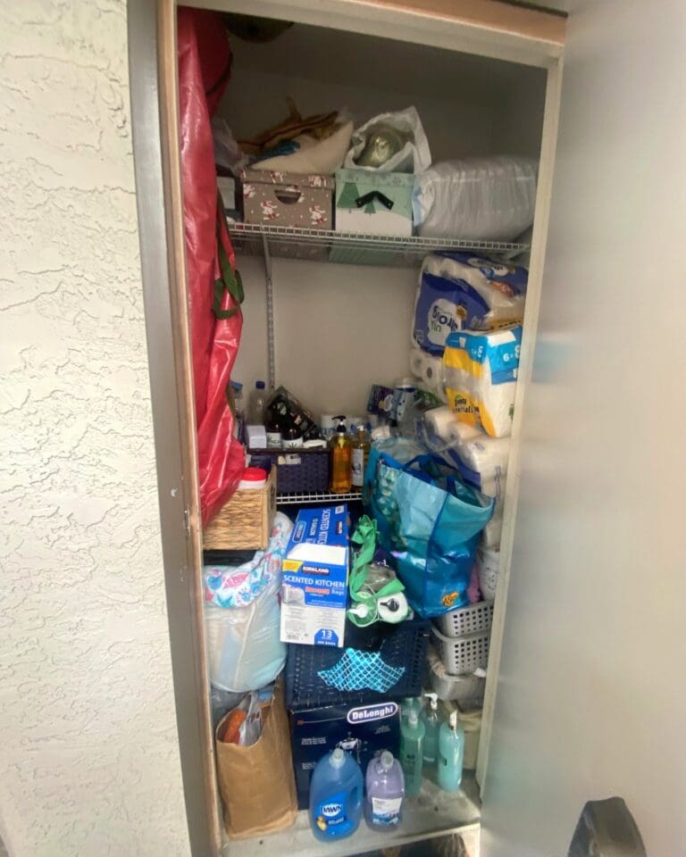 Orange County storage closet before decluttering, with paper towels, cleaning supplies, bags and boxes crammed onto wire shelves and the floor