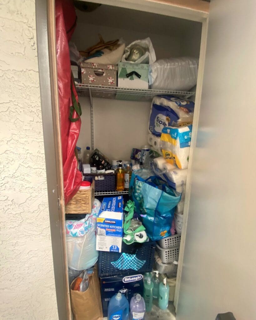 Storage closet before decluttering, packed floor to ceiling with paper goods, bags and cleaning supplies