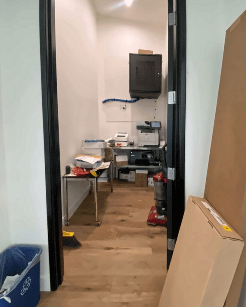 Commercial office supply room before organizing, with a cluttered table and boxes in the doorway