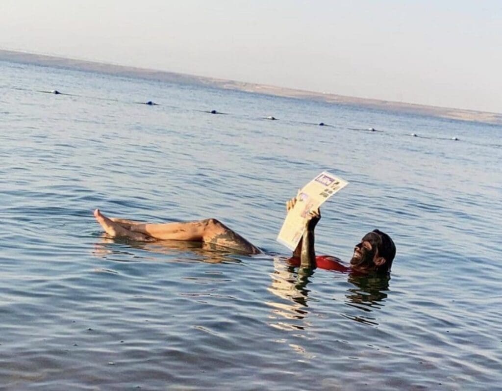 A person floating with feet up in calm water during sunset.