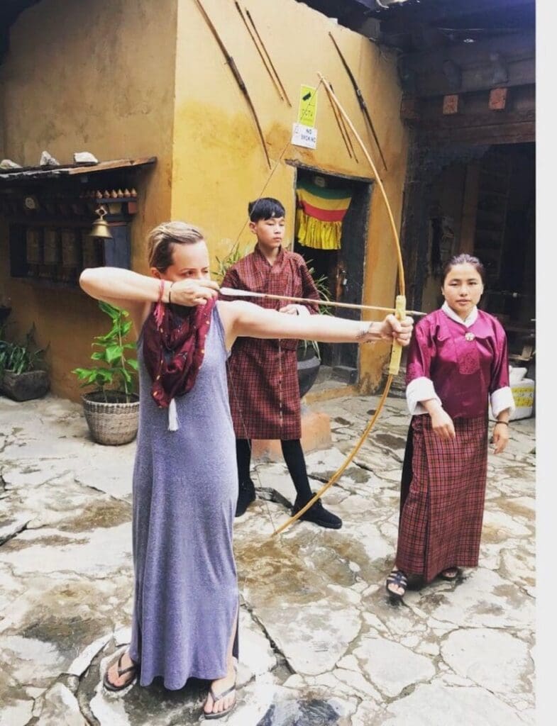 Three women in traditional attire holding a long bamboo stick outdoors.