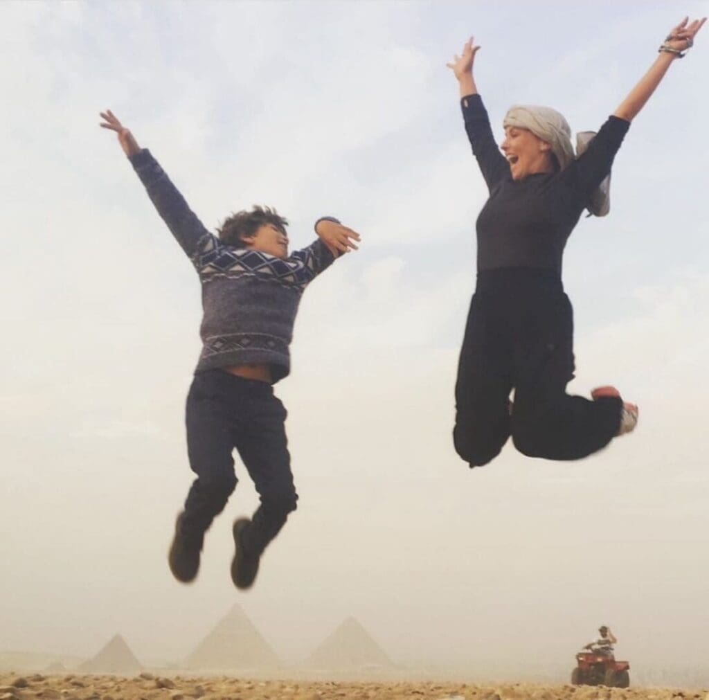 Two people joyfully jumping with pyramids in the background.