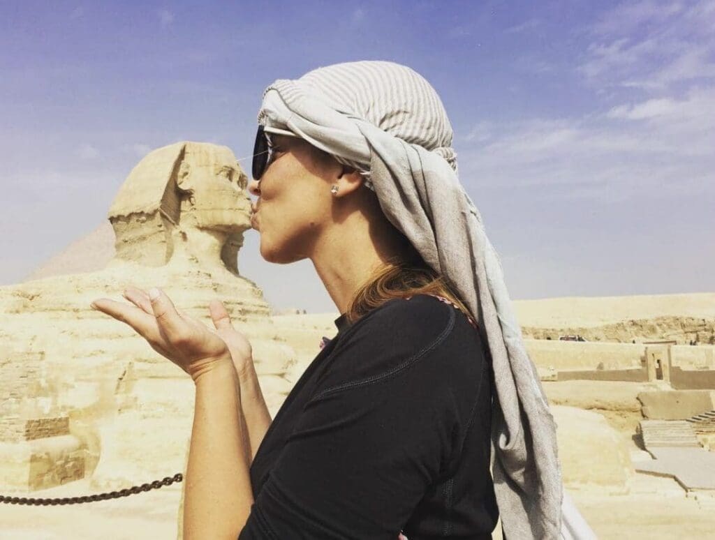 A woman appears to kiss the Great Sphinx of Giza in a playful perspective photo.