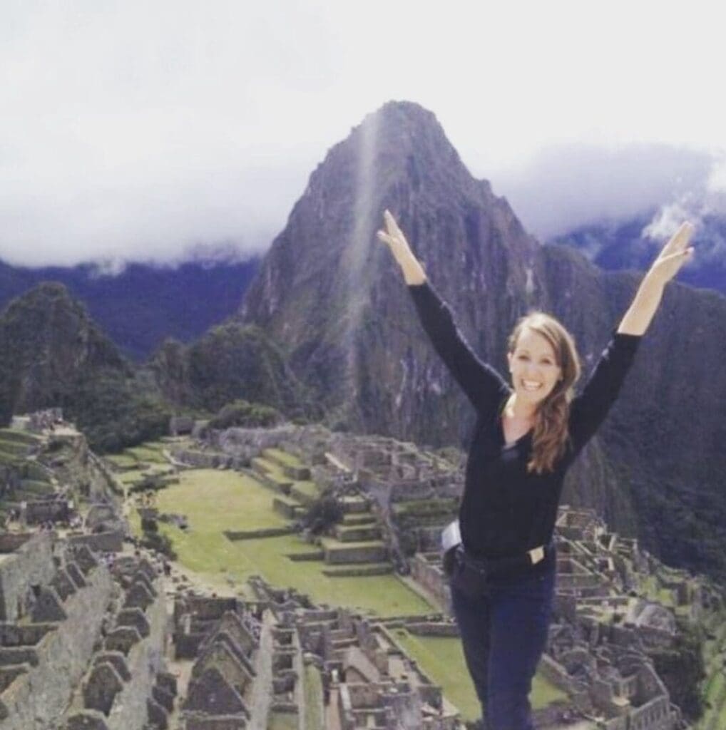 Woman posing happily at Machu Picchu with arms raised.