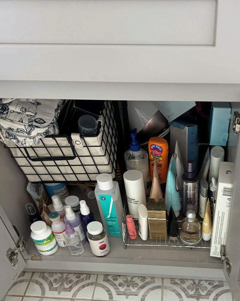 Bathroom under-sink cabinet before organizing, with toiletries piled in wire baskets, Costa Mesa