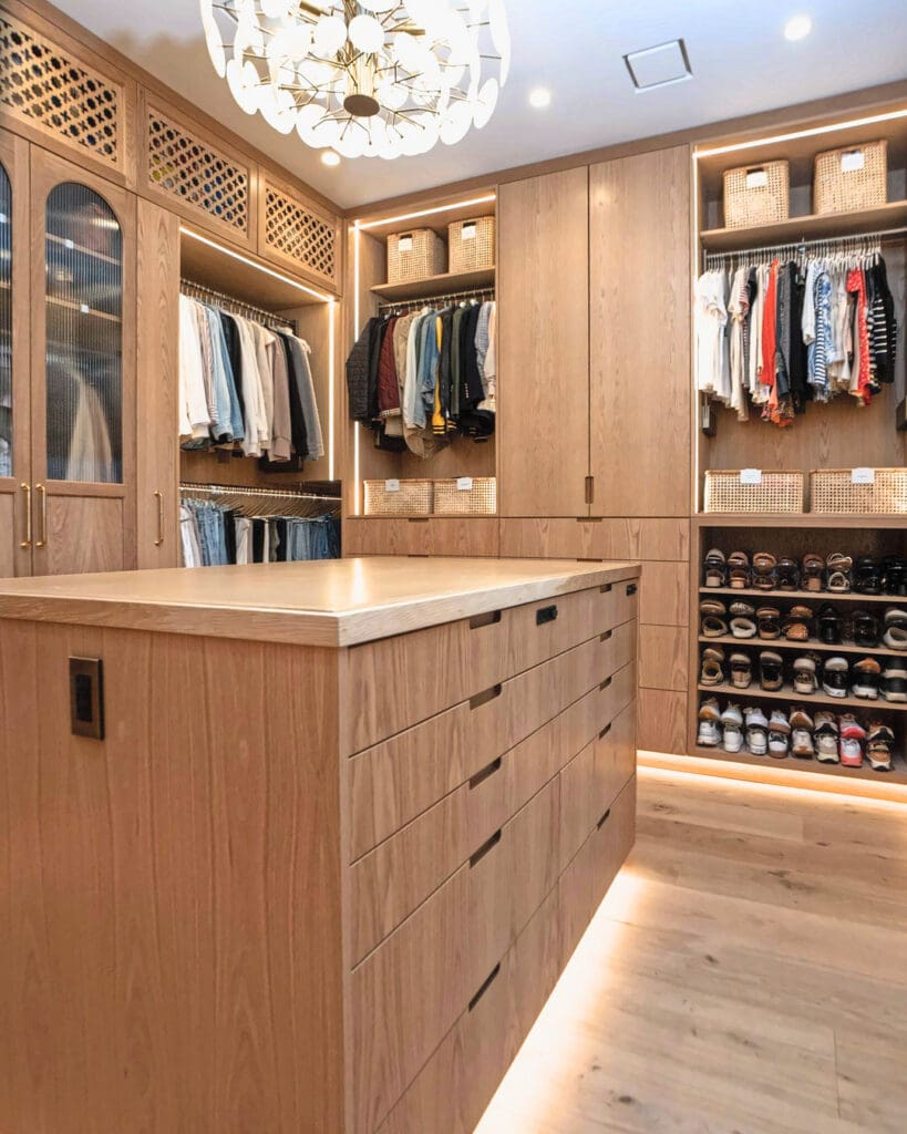 Same walk-in closet after Simply Luxe organizing, with clothes hung by color, baskets up top and a softly lit drawer island, San Diego