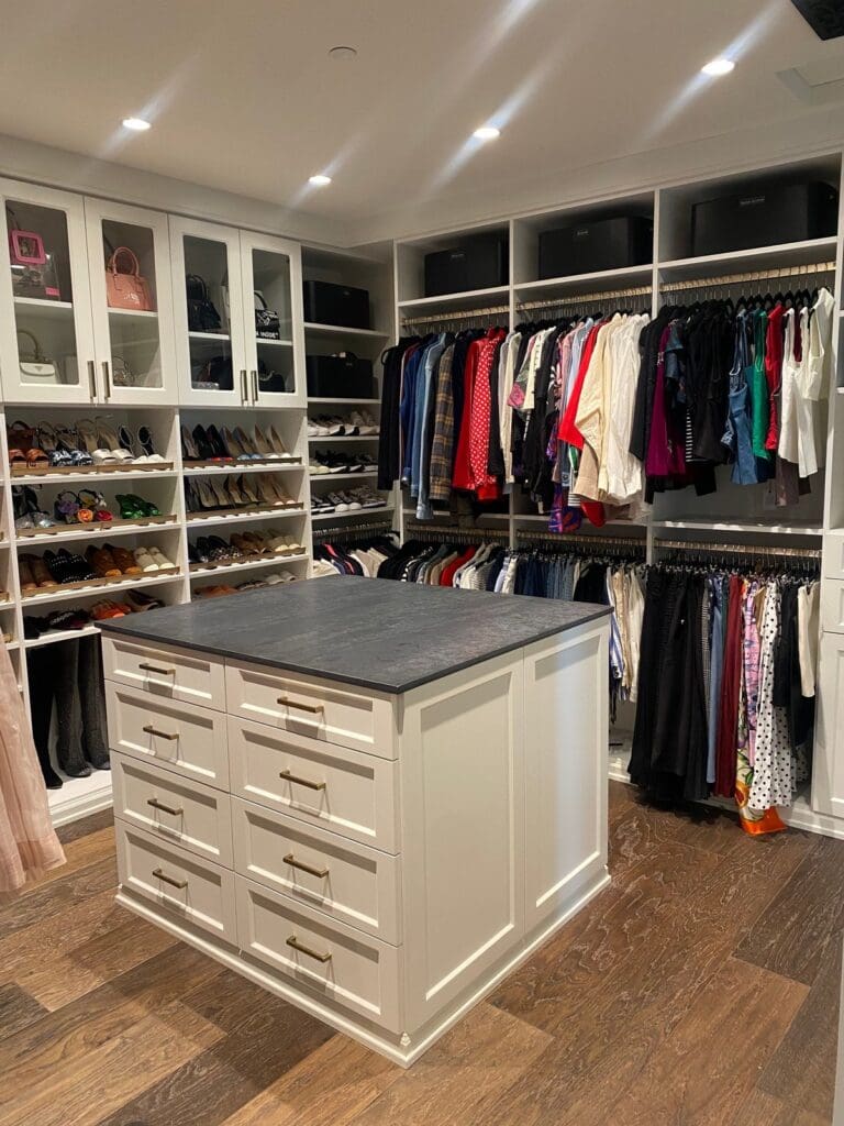Walk-in closet with a center island, glass-front handbag cabinets and color-sorted hanging clothes, organized in San Diego