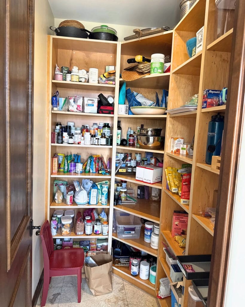 Walk-in pantry before organizing, with crowded shelves, supplements and a red chair on the tile floor, Solana Beach home