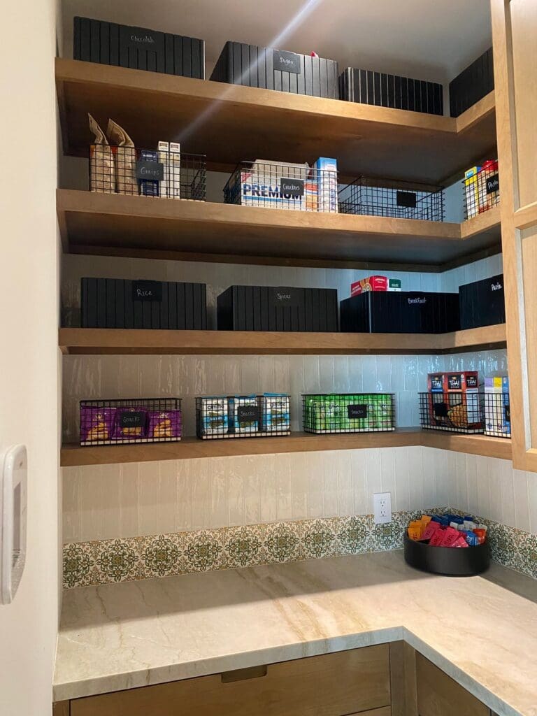 Walk-in pantry with labeled black bins and wire snack baskets on open wood shelves, organized in San Diego
